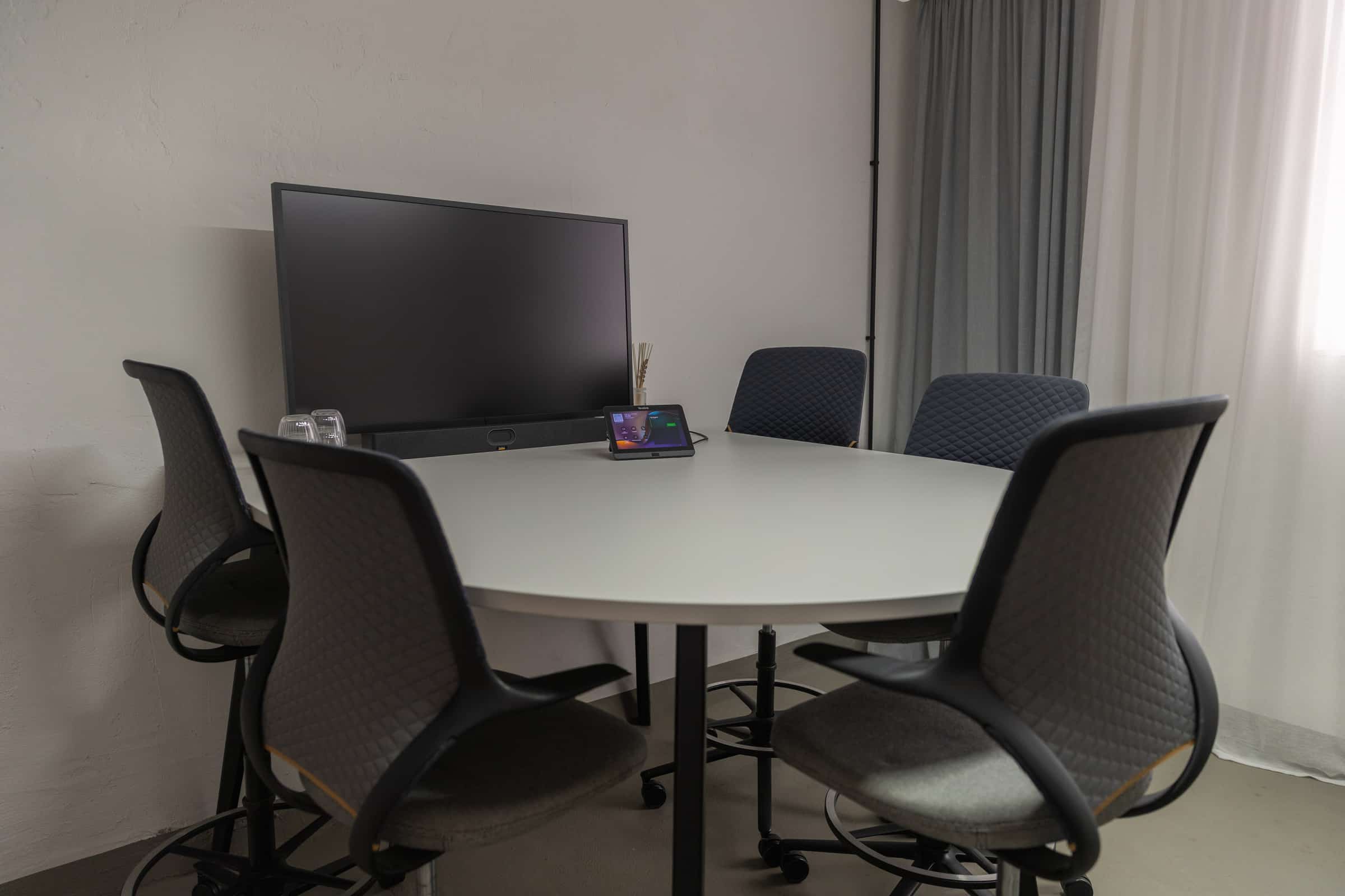 Besprechungsraum mit rundem Hochtisch und Bildschirm
